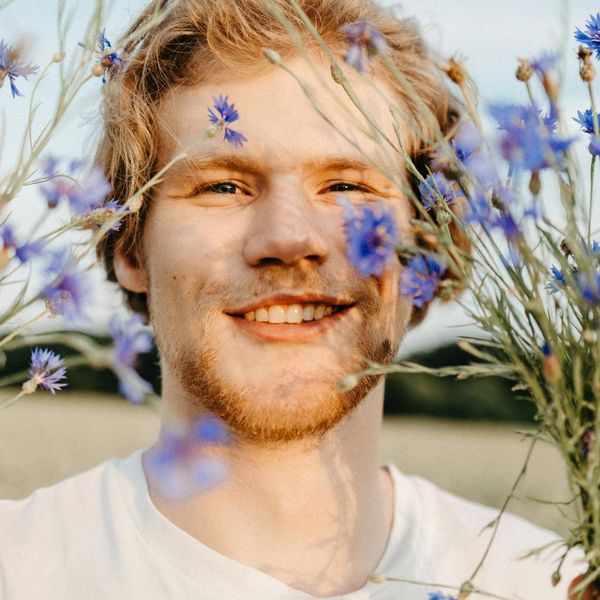 Person smiling and stretching in a sunlit natural environment.